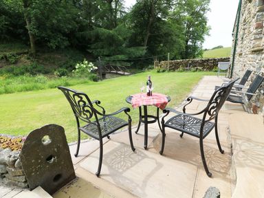 A patio with two metal chairs and a small table with a bottle of wine and glasses on a lawn at Grayrigg Foot Stable in Grayrigg