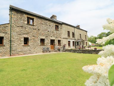 A stone and plaster house with wooden windows and a green lawn at Grayrigg Foot Stable in Grayrigg