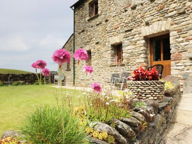 A stone house with wooden doors and windows and a garden with flowers and stone planters at Grayrigg Foot Stable in Grayrigg