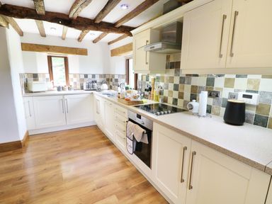 A kitchen with wooden beams on the ceiling white cabinets and tiled backsplash at Grayrigg Foot Stable in Grayrigg