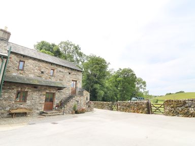 A stone building with wooden doors and windows beside a stone wall and green field at Grayrigg Foot Stable in Grayrigg