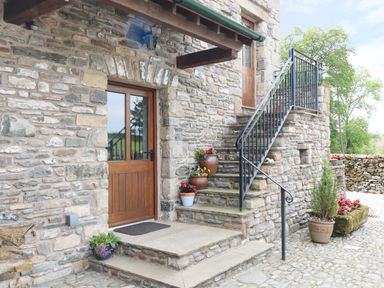 Stone building exterior with wooden doors stone steps and potted plants at Grayrigg Foot Stable in Grayrigg