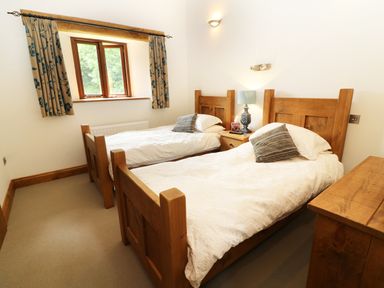 A bedroom with two wooden single beds a window with curtains and a bedside table with a lamp at Grayrigg Foot Stable in Grayrigg
