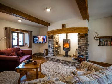 A living room with a wood burning stove in a stone fireplace a wooden coffee table and two sofas at Grayrigg Foot Stable in Grayrigg