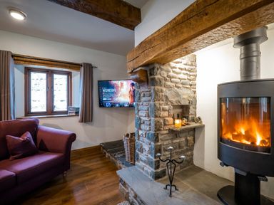 A living room with a stone fireplace a wood burning stove a purple sofa and a TV mounted on the wall at Grayrigg Foot Stable in Grayrigg
