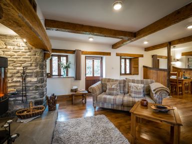 A living room with a plaid sofa wooden coffee table stone fireplace and dining area at Grayrigg Foot Stable in Grayrigg