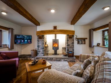 A living room with a stone fireplace wood stove wooden beams and a television at Grayrigg Foot Stable in Grayrigg