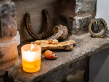 A stone hearth surface with a lit candle a wooden mouse a wooden carved decoration a horseshoe and a sundial at Grayrigg Foot Stable in Grayrigg