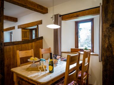 A dining area with a wooden table and chairs a bottle of prosecco and two glasses with food on the table at Grayrigg Foot Stable in Grayrigg