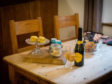A wooden table with a bottle of prosecco and two glasses with drink biscuits and cans and a bowl of crisps at Grayrigg Foot Stable in Grayrigg