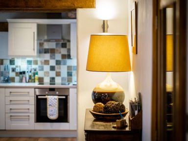 A kitchen with white cabinets an oven and a tiled backsplash next to a table with a lamp and decorative balls at Grayrigg Foot Stable in Grayrigg