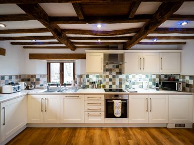 A kitchen with white cabinets wooden beams on ceiling and tiled backsplash at Grayrigg Foot Stable in Grayrigg