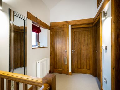 A hallway with wooden doors a window with a red blind a radiator and a wall mirror at Grayrigg Foot Stable in Grayrigg