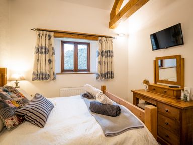 A bedroom with a bed pillows bedside lamp wooden dresser mirror and a TV on the wall at Grayrigg Foot Stable in Grayrigg