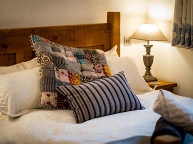 A bed with white bedding two decorative pillows a wooden headboard and a bedside table with a lamp at Grayrigg Foot Stable in Grayrigg