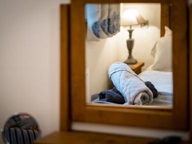 A bedroom with rolled towels on a bed and a lamp on a bedside table reflected in a wooden framed mirror at Grayrigg Foot Stable in Grayrigg