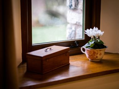 A wooden windowsill with a wooden box and a floral teacup holding white flowers at Grayrigg Foot Stable in Grayrigg