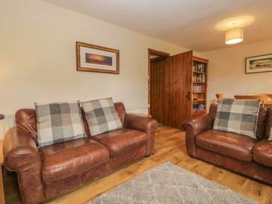 A living room with two brown leather sofas and plaid cushions a wooden door and a bookcase at Tanner Croft Cottage in Grasmere