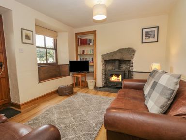 A living room with a leather sofa a stone fireplace a window seat and a small television at Tanner Croft Cottage in Grasmere