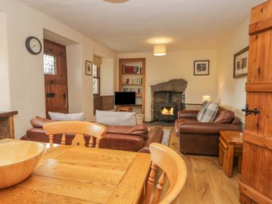 A living room with a wood burning stove two brown leather sofas a wooden dining table and chairs and bookshelves at Tanner Croft Cottage in Grasmere