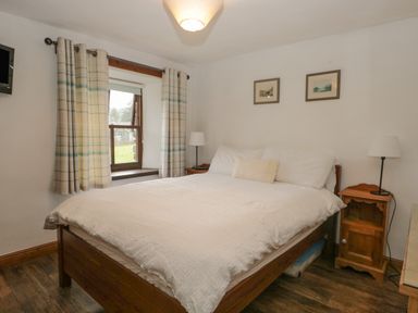 A bedroom with a wooden bed white bedding two bedside tables with lamps and a window with curtains at Tanner Croft Cottage in Grasmere