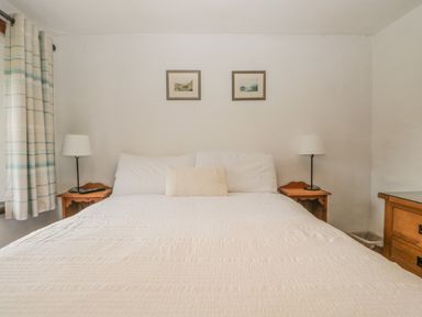 A bedroom with a bed white bedding two bedside tables with lamps two framed pictures on the wall and a window with curtains at Tanner Croft Cottage in Grasmere