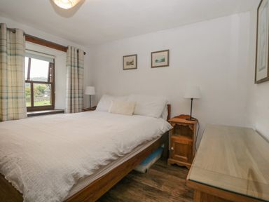 A bedroom with a double bed bedside tables lamps window with curtains and framed pictures on the wall at Tanner Croft Cottage in Grasmere