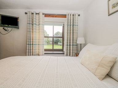 A bedroom with a bed a pillow a window with curtains a lamp and a wall-mounted television at Tanner Croft Cottage in Grasmere