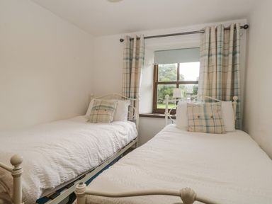 A bedroom with two single beds white bedding plaid pillows and plaid curtains at Tanner Croft Cottage in Grasmere