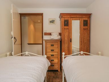 A bedroom with two single beds a wooden chest of drawers and a wooden wardrobe at Tanner Croft Cottage in Grasmere