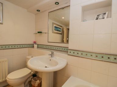 A bathroom with a toilet sink mirror and tiled walls at Tanner Croft Cottage in Grasmere