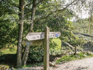 A wooden signpost indicating directions to Grasmere and Ambleside with trees and a stone wall in the background at Tanner Croft Cottage in Grasmere
