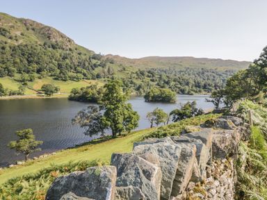 A stone wall with a lake and hills covered with trees in the background at Tanner Croft Cottage in Grasmere