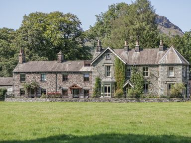 Stone cottages with multiple chimneys surrounded by green trees and grass at Tanner Croft Cottage in Grasmere