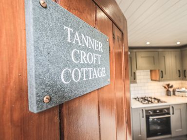 A kitchen with grey cabinets a gas stove and oven and a wooden door with a sign saying Tanner Croft Cottage in Grasmere