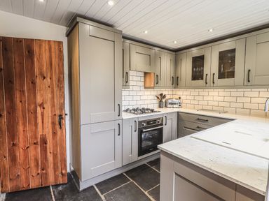 A kitchen with grey cabinets a wooden door a built in oven and a white countertop at Tanner Croft Cottage in Grasmere
