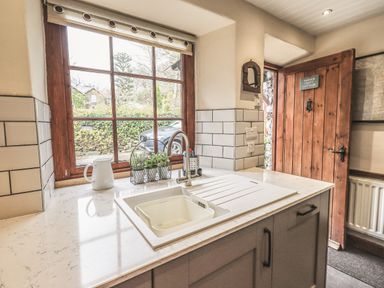A kitchen sink with a faucet next to a window and a wooden door at Tanner Croft Cottage in Grasmere