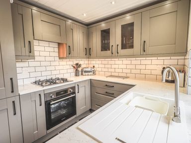 A kitchen with grey cabinets white tiled backsplash gas stove oven toaster and sink at Tanner Croft Cottage in Grasmere