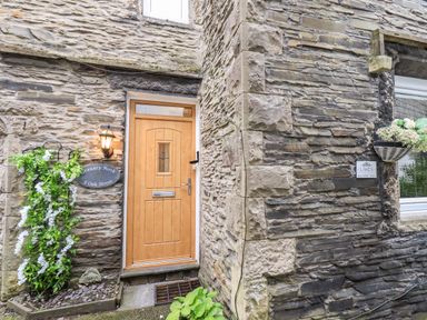 Stone exterior wall with a wooden door and a window with flower baskets at Granary Nook in Windermere