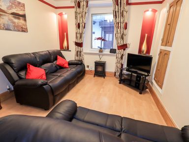 A living room with black leather sofas red pillows a television on a stand and curtains at Granary Nook in Windermere