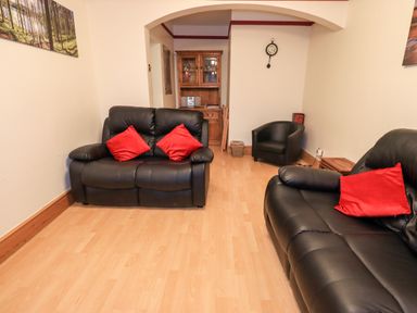 A living room with black leather sofas red cushions a wooden cabinet and a wall clock at Granary Nook Windermere
