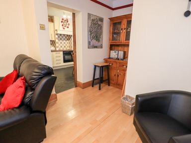 A living room with black leather chairs red cushions wooden cabinet and stools next to a kitchen at Granary Nook in Windermere