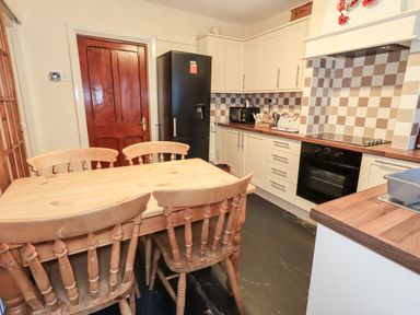 A kitchen with a wooden dining table and chairs a black refrigerator and white cabinets at Granary Nook in Windermere