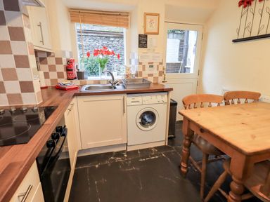 A kitchen with dishwasher washing machine sink wooden table and chairs at Granary Nook in Windermere