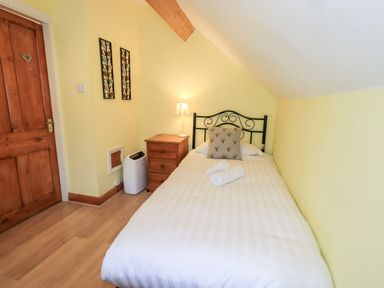 A bedroom with a single bed a wooden nightstand with a lamp a wooden door and wall decorations at Granary Nook in Windermere