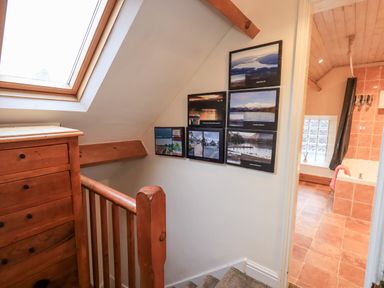 A staircase landing with wooden railing and dresser next to a wall with framed pictures and a view into a bathroom at Granary Nook in Windermere