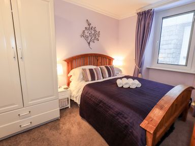 A bedroom with a wooden bed with pillows and rolled towels a white wardrobe and a window at Granary Nook in Windermere