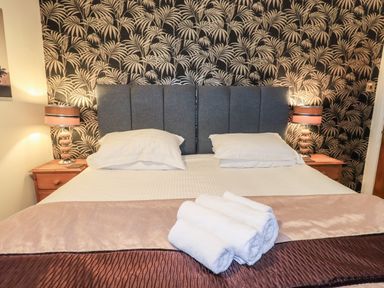 A bedroom with a bed with two pillows and a folded towel on it two bedside tables with lamps and a patterned wallpaper at Granary Nook in Windermere