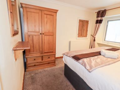 A bedroom with a wooden wardrobe a bed with folded towels and a window with curtains at Granary Nook in Windermere