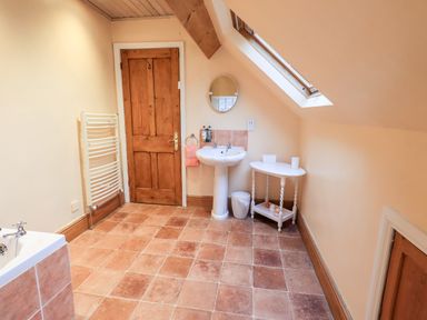 A bathroom with a sink mirror wooden door small table and a skylight window at Granary Nook in Windermere